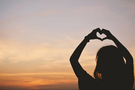 妇女在天空日落背景心形的剪影手照片