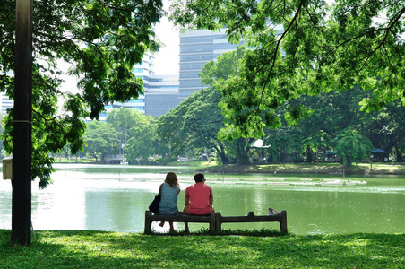 夫妻爱在岩石大湖旁的长凳上坐在一起