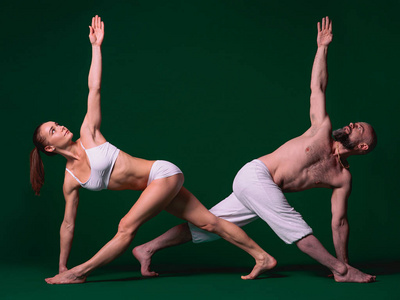 美丽的运动妇女和男子在白色的衣服做瑜伽体式在室内绿色背景