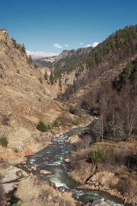 一幅风景如画的图片, 描绘了俄罗斯北部高加索地区的峡谷景观, 一条横跨落基山脉的河流, 绿树成荫, 蓝天密布。