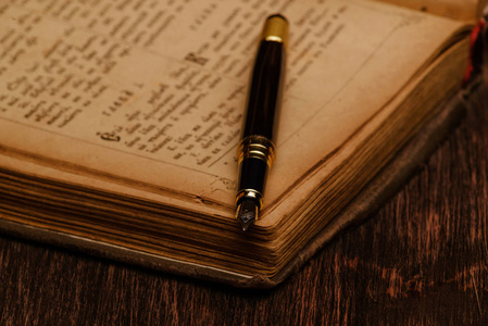 一本旧书和一支钢笔在木质背景上