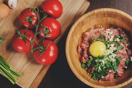 原始肉末鸡蛋，香草和新鲜的西红柿，木制的桌子上。成分为烹饪肉丸子或乡村厨房里的面包