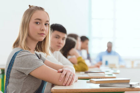 白人女学生的肖像坐在办公桌上与同学和老师背后