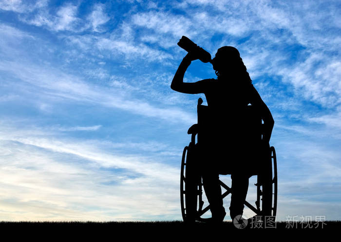一个残疾妇女的剪影在轮椅饮用水从塑料瓶
