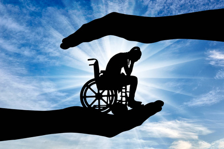 轮椅上的悲伤残疾妇女的剪影在帮助之下