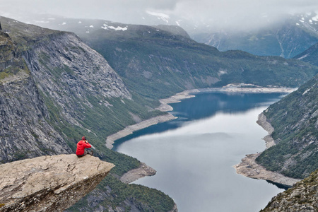 男人坐在 Trolltunga 岩石 巨魔的舌头岩 的相机，使与挪威山风景照片