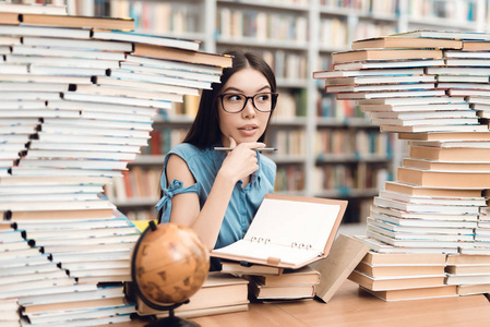 亚洲女孩坐在桌边的桌子旁, 四周是图书馆的书和笔记本上的写字。