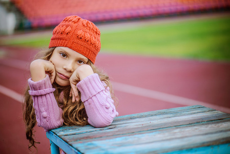 在体育场上戴着红色帽子的小美丽女孩