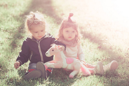 在阳光明媚的日子里, 女孩和男孩玩玩具马。姐姐和哥哥坐在绿草上。家庭, 爱, 信任。孩子朋友友谊儿童, 童年概念