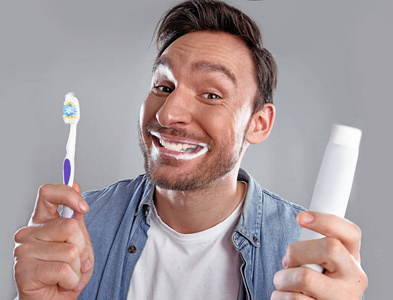 英俊滑稽胡子的人在白色衬衫是痴迷于他的牙齿健康他用牙膏和牙刷擦得很硬, 现在他很高兴。