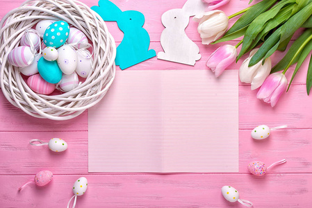 复活节彩蛋在一个柳条篮子和一束郁金香在粉红色的背景。复活节节日贺卡
