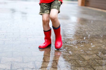 儿童穿红色雨靴跳进水坑