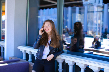 在街道咖啡馆窗口附近用智能手机交谈的年轻女性人