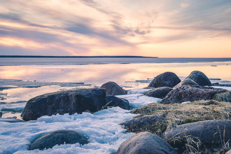 夕阳的抽象形象, 在湖面上融化的冰在早春。金黄小时颜色草和石头