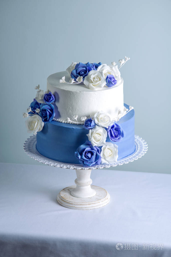 美丽的两个分层的白色和蓝色婚礼蛋糕装饰花糖玫瑰.优雅假日甜点概念