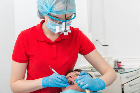 照片的牙医在面具与放大镜双筒望远镜治疗病人的牙齿