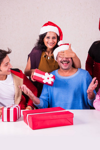 圣诞节的时候，快乐印度家庭坐在桌子对面和交换圣诞礼物戴圣诞老人帽子帽，圣诞快乐，印度家庭庆祝圣诞节