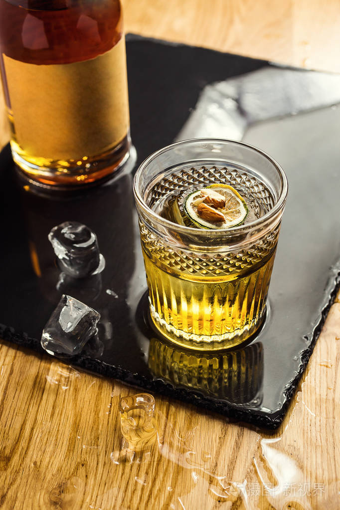 杯威士忌 (白兰地或白兰地) 与柠檬和冰块站在酒吧柜台上的背景瓶子