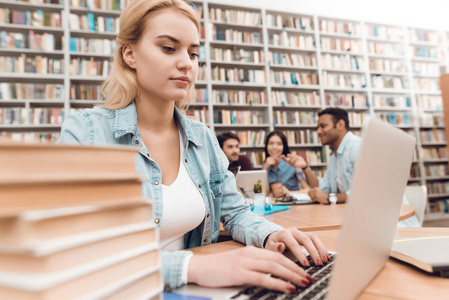 一群多文化的学生坐在图书馆的桌子上, 白人女孩在笔记本电脑上工作