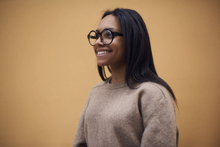 美丽的微笑美国黑人女性在眼镜站在宣传背景下, 有吸引力的欢快的深色皮肤模型在毛衣享受自由时间梦想的东西在宣传领域