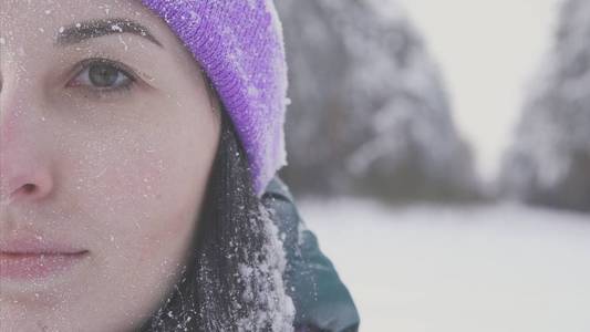 戴着紫色帽子的女孩看着在冬季森林的背景下的相机, 霜