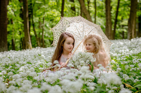 两个美丽的孩子坐在草地下的伞