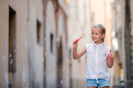 可爱的小女孩，在户外吹肥皂泡泡在欧洲城市。肖像的白种人的孩子享受暑假在意大利