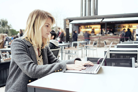 年轻迷人的妇女在户外咖啡馆工作的笔记本电脑
