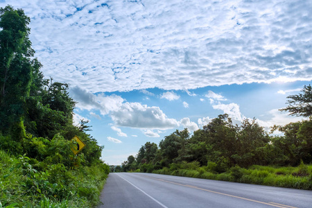 农村公路蓝色的天空和云，绕过一片绿森林