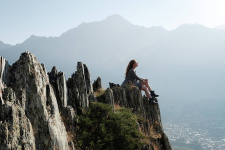 一个穿着飞天连衣裙的漂亮女孩坐在俯瞰群山的悬崖上.照片