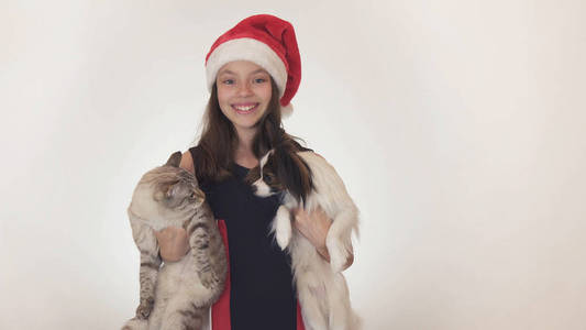美丽的少女在圣诞老人帽子拥抱她的猫和狗在白色背景
