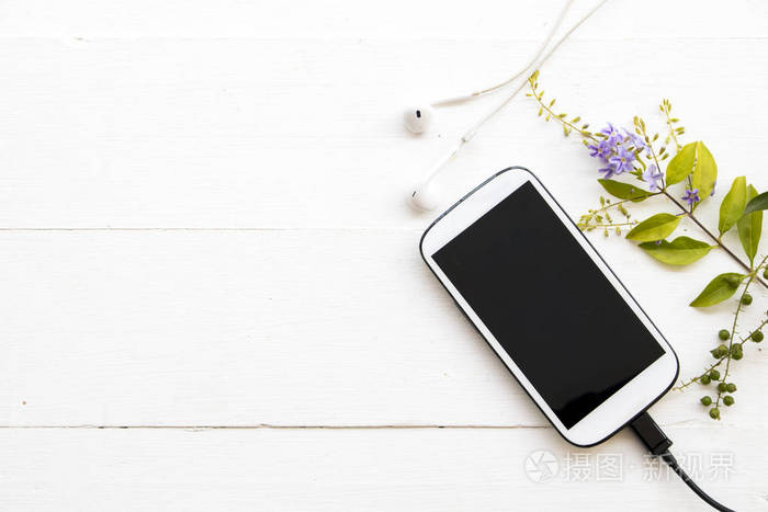 白色手机耳机和可充电电池线与紫色花在背景木白色