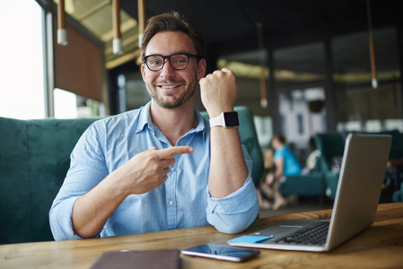 微笑的商人肖像满意现代数码设备手腕显示 smartwatch 与触摸屏, 繁荣的企业家享受使用方便 smartwatch 在工作