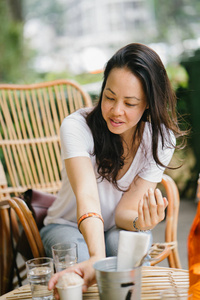 一个泛亚洲女人的肖像, 在咖啡和冰淇淋的咖啡馆里, 在阳光下放松。她坐在藤椅上, 微笑着, 而她享受下午