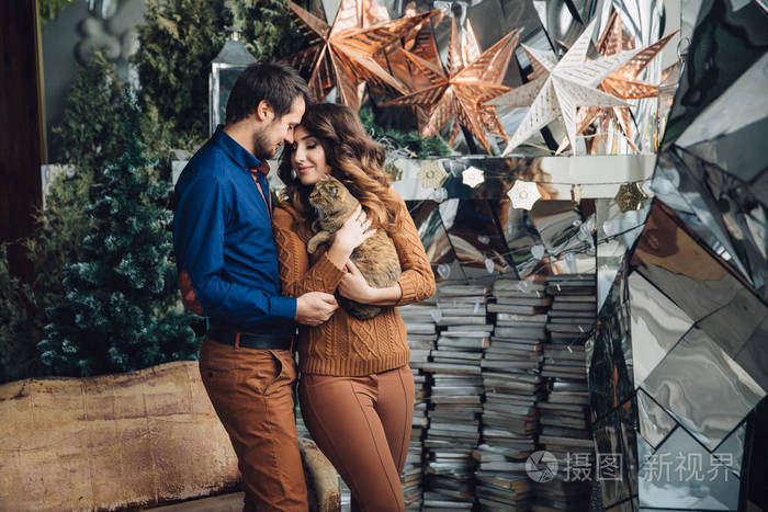 美丽热恋中的情侣和一只猫在他们的怀里坐在沙发上拥抱微笑和亲吻家庭