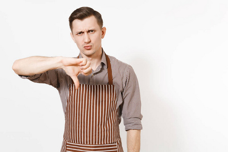 年轻的伤心不安的人厨师或服务员在条纹棕色围裙, 衬衫显示拇指向下孤立的白色背景。男管家或 houseworker 看相机。家政工