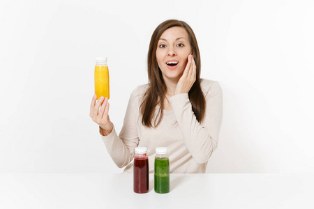 在餐桌上的年轻妇女与绿色, 红色和黄色的排毒冰沙酒瓶在白色背景隔离。适当的营养, 素食饮料, 健康的生活方式, 节食的概念。具有