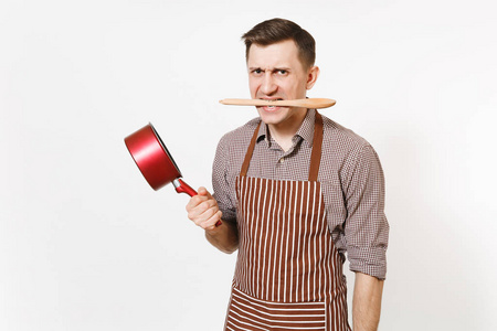 进取的人厨师或服务员在条纹褐色围裙, 衬衣拿着红色空的 stewpan, 木勺在嘴被隔绝在白色背景。男管家或 housework