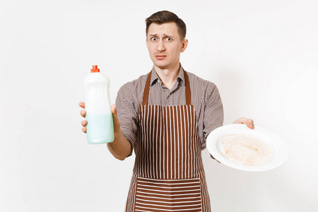 男子在条纹棕色围裙, 衬衫持有白色圆形脏盘子, 洗涤剂。用干净的液体在白色背景下的瓶子里洗盘子。男管家houseworker 
