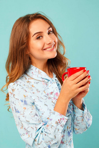 在蓝色背景下拿着一杯茶或咖啡的年轻女子