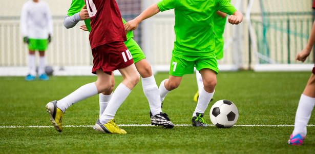 男孩踢足球场足球比赛。运行年轻足球运动员。孩子们在运动场上玩足球比赛
