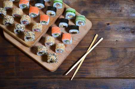 一张日本寿司卷的详细照片和他们使用的设备 筷子, 它们位于寿司酒吧厨房餐桌上的木制裁剪板上。