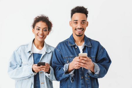 快乐的非洲夫妇在牛仔衬衫持有他们的智能手机