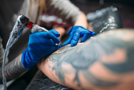 女性 tattooist 在男性肩上用机器做纹身。沙龙专业纹身