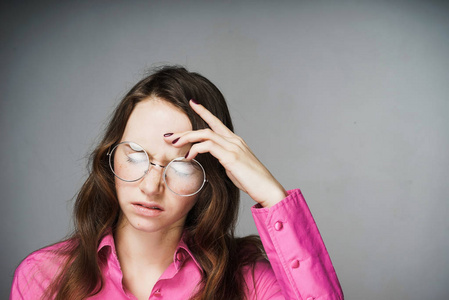 疲惫的年轻女子办公室工作人员在粉红色的衬衫和眼镜闭上眼睛, 头痛