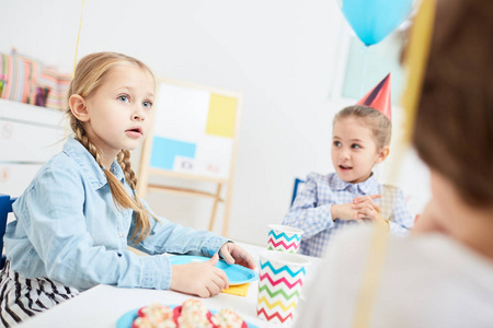 可爱的小孩子与纸盘子坐在节日桌在幼稚园和谈话对朋友