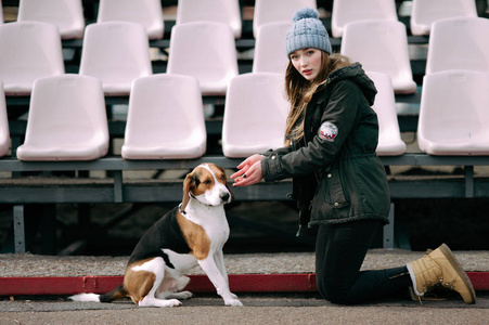 年轻的时髦女孩与她的宠物爱沙尼亚猎犬狗玩，俊平和拥抱和室外在玩老体育场