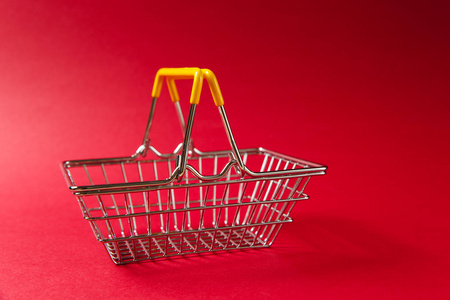 在超市里, 用凸起的手柄和红色背景上的黄色塑料元素, 关闭金属购物篮。购物的概念。复制广告空间