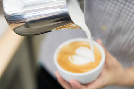 女咖啡壶浇流牛奶制作拿铁艺术咖啡与心脏形状在白色杯子, 选择和柔和的焦点