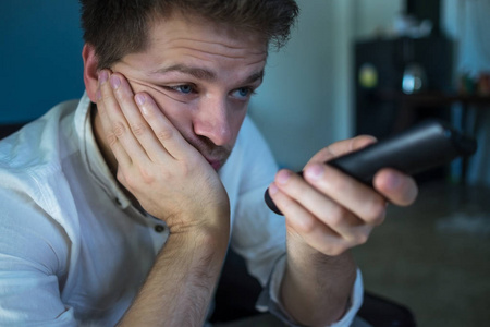 无聊的电影无聊的白种人看电视和电击坐在家里或酒店的沙发上照片